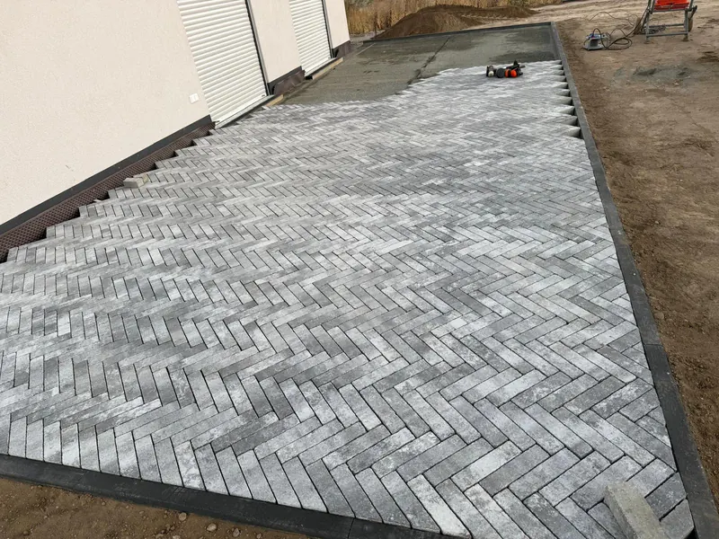 Langformatiges Pflaster im Fischgrätverband vor einem Neubau mit Kiesstreifen